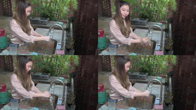 一名亚洲华裔女性在晚宴后在厨房的盆子里洗碗，用自来水洗水杯