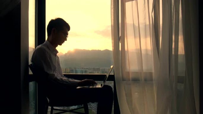 男人坐在窗户上的笔记本电脑上打字