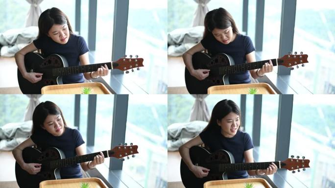 一位亚洲华裔小姐闲暇时在家弹吉他，爱好愉快