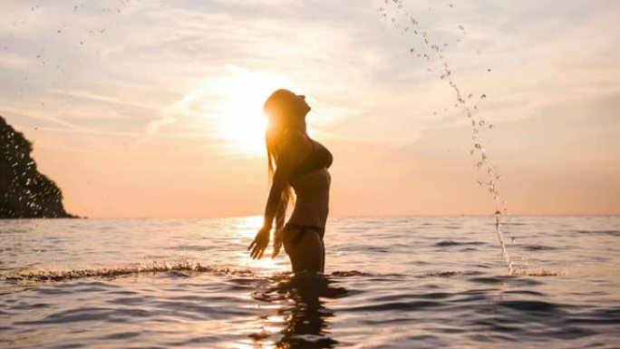 暑假穿着比基尼的女人站在海水中，用长长的湿头发和泼水做头发翻转