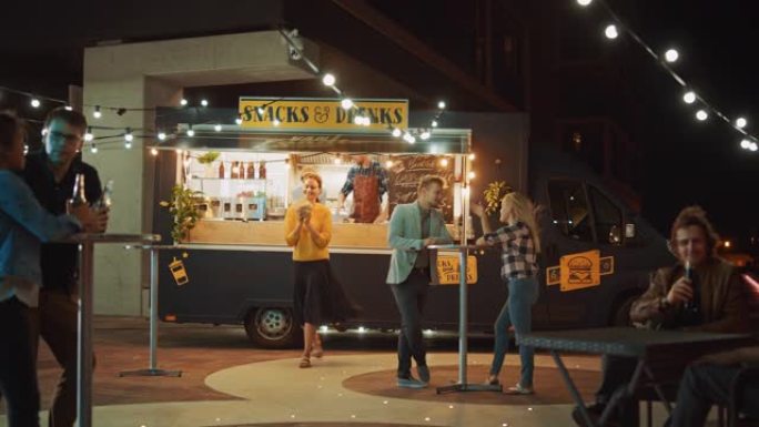 食品卡车员工将汉堡交给快乐美丽的年轻时髦顾客。成功的食品卡车员工给击掌。在现代凉爽的街区出售街头食品