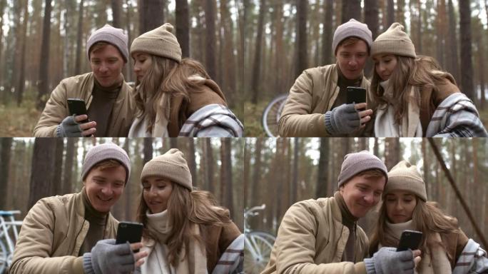 快乐的情侣在秋天的日子里使用智能手机在森林里聊天