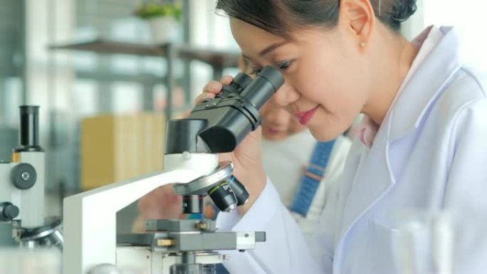 亚洲小孩，老师在学校实验室里用显微镜看。小女孩用显微镜学习科学课。教育主题