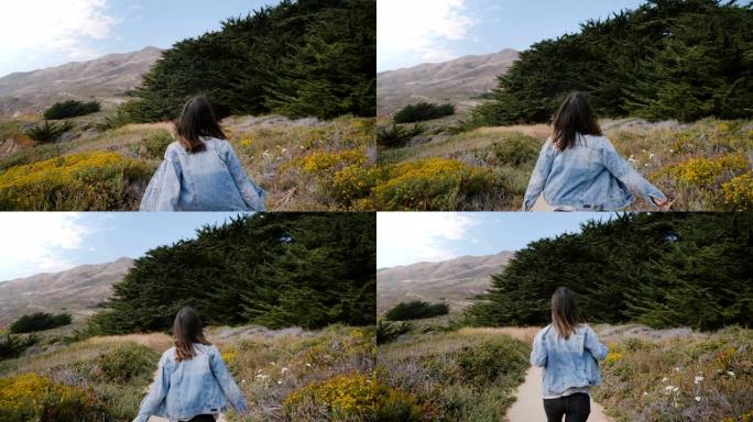 镜头跟随年轻快乐的女人沿着一条小路奔向加利福尼亚大苏尔海岸线的大石头和森林