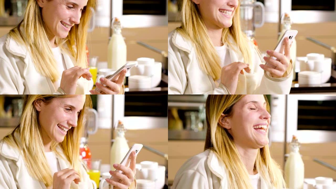 一个女人在厨房里吃早餐，喝着茶杯或牛奶，用电话发送消息或打电话，并微笑。