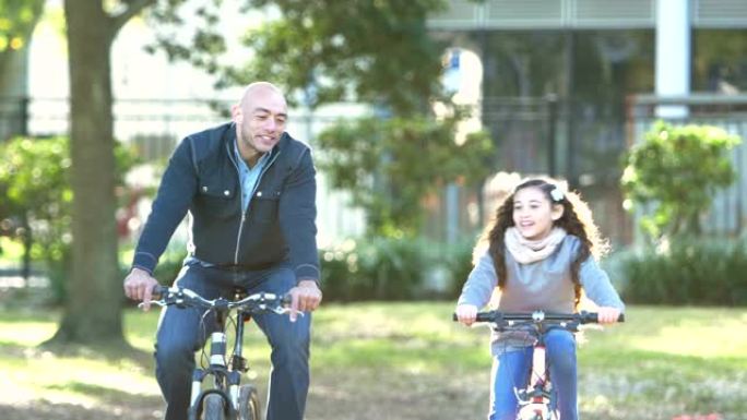 西班牙裔父亲和女儿在公园骑自行车