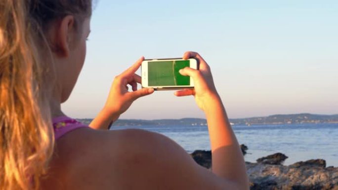 经过岩石海岸训练。女孩用绿屏检查她的智能手机