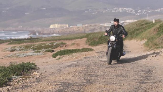 英俊的骑自行车的人骑着经典的摩托车在海边