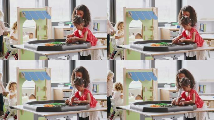 年轻的女学生在幼儿教室里与女老师站在感官游戏桌旁