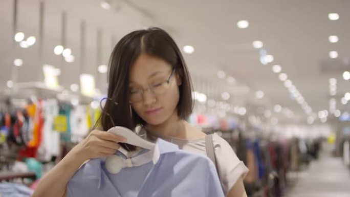 亚洲女性在商店里的衬衫和摆姿势拍照之间进行选择