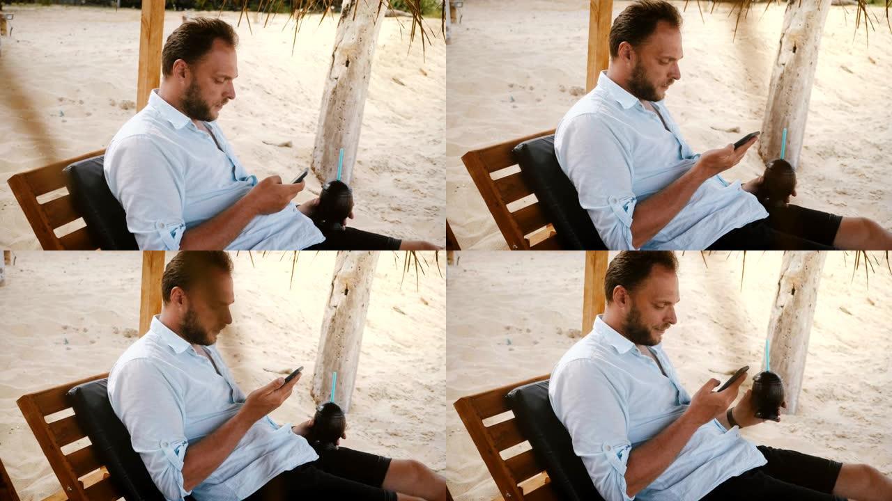 快乐自信的男性游客，智能手表和水果鸡尾酒坐在沙滩椅上，使用智能手机社交网络