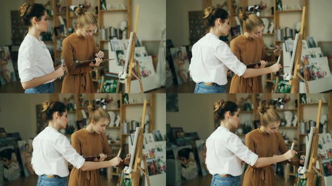 勤奋的学生在现代工作室的专业艺术家的指导下绘画。女人指着画布并提供建议。