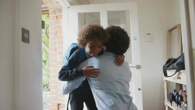 穿着时髦的中年黑人男子跪在前门的走廊上拥抱并告别儿子，然后他早上去上学，角度低