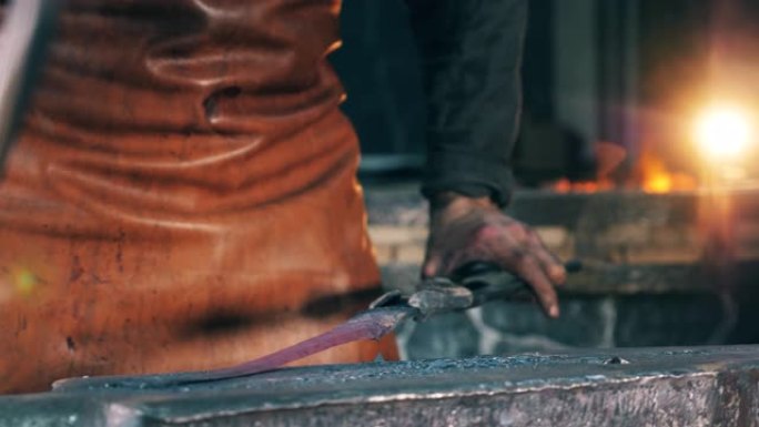 一个人撞击金属物体，用铁锤在锻造炉上塑造它。