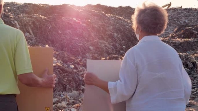 描绘一对亚洲老年夫妇站在来自亚洲垃圾填埋场的巨大垃圾堆上，手持环保运动人士为大自然而战的海报。志愿服