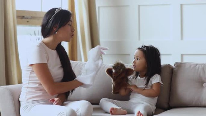 可爱的亚洲小女孩戴着皇冠和妈妈玩木偶