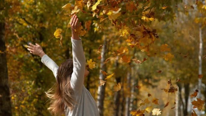 特写: 女人在空中扔了一堆树叶后伸出双臂。