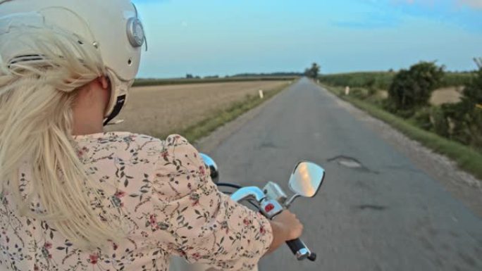 黄昏时在乡间小路上骑踏板车的女人的SLO MO肖像