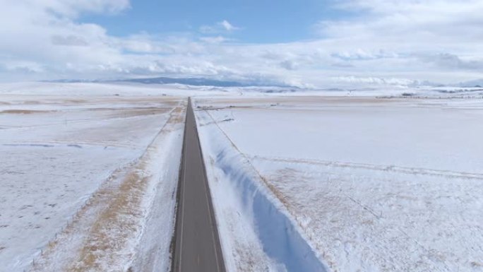 空中: 沿着空的沥青高速公路穿越蒙大拿州的白雪皑皑的平地飞行
