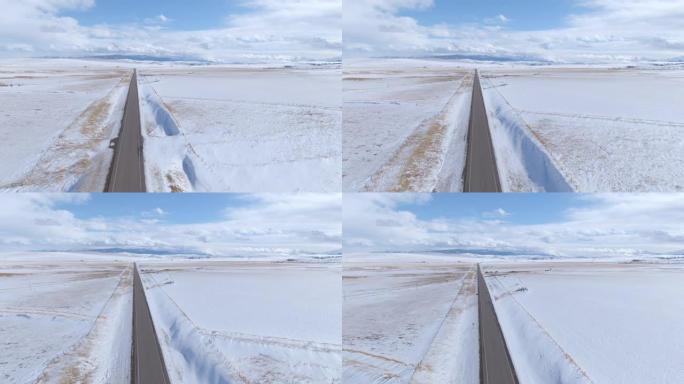 空中: 沿着空的沥青高速公路穿越蒙大拿州的白雪皑皑的平地飞行