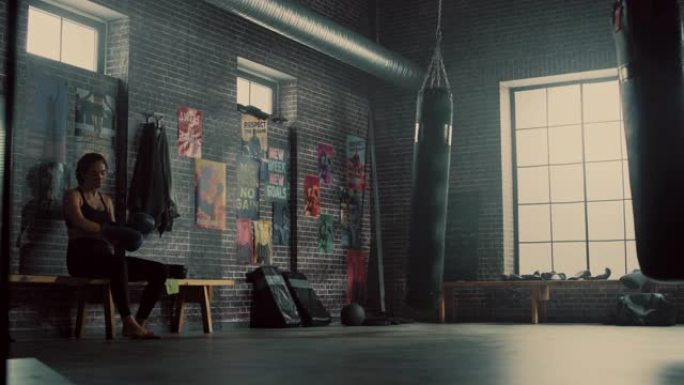 美丽健康的黑发跆拳道运动员坐在阁楼健身房的长凳上，用激励海报。她屏住呼吸，脱下战斗手套。经过紧张的训