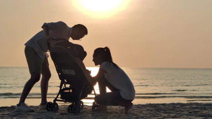 剪影快乐的父亲，母亲，宝贝儿子在沙滩上沿着日落海上冲浪的边缘充满乐趣。活跃的父母和人们在暑假与婴儿一