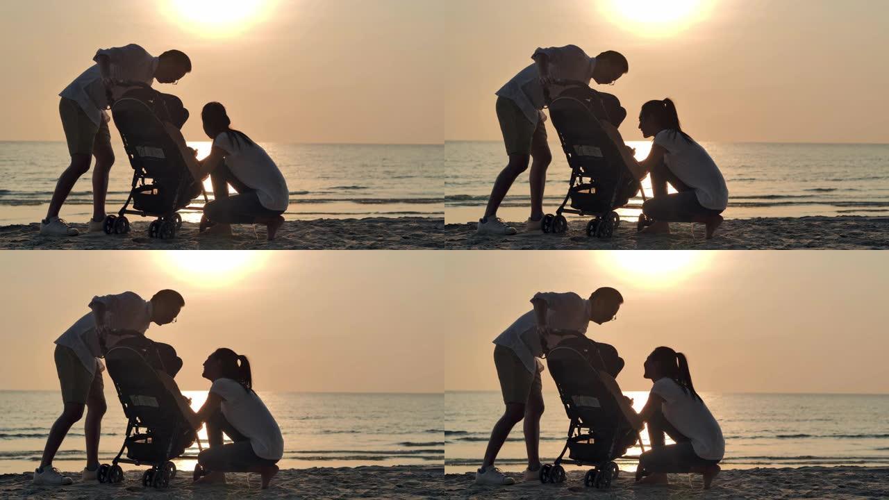 剪影快乐的父亲，母亲，宝贝儿子在沙滩上沿着日落海上冲浪的边缘充满乐趣。活跃的父母和人们在暑假与婴儿一