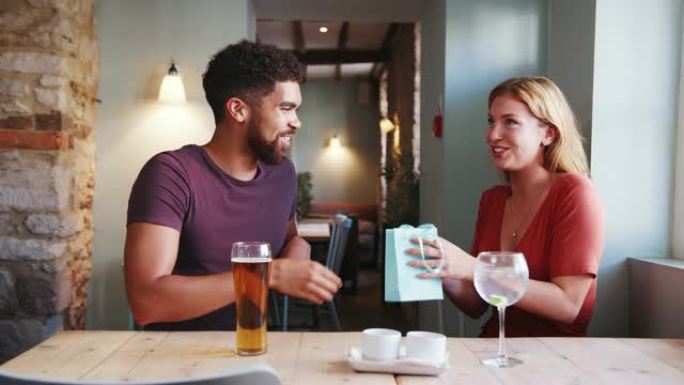 快乐的年轻成年女性对男友的礼物感到惊讶，当时他们坐在酒吧里喝酒，特写镜头