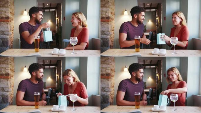 快乐的年轻成年女性对男友的礼物感到惊讶，当时他们坐在酒吧里喝酒，特写镜头