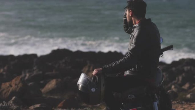 英俊的男人穿着皮夹克骑着摩托车在海边