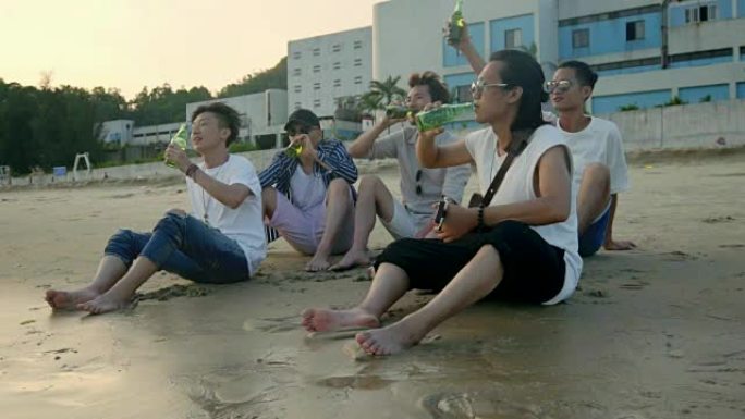 年轻的亚洲成年人坐在海滩上放松，喝啤酒敬酒