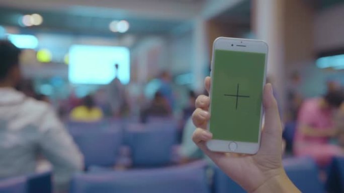 亚洲妇女在国际机场使用带有绿屏的白色手机设备。