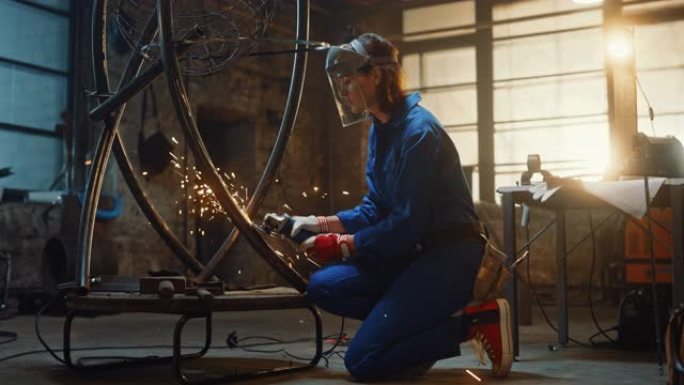 穿着蓝色连身裤的年轻当代女艺术家正在工作室里用角磨机打磨一个金属管雕塑。赋权女人用金属制作现代残酷的