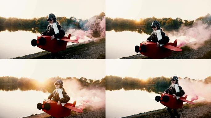 快乐的小飞行员女孩穿着有趣的飞机服装在日落湖边跑步，镜头中彩烟闪耀慢动作