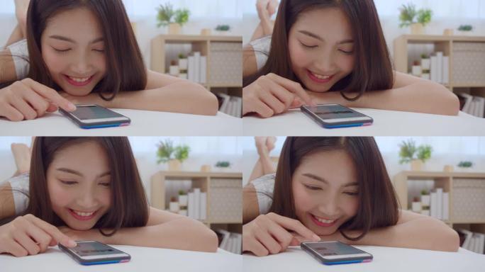 慢动作-年轻的亚洲女性使用智能手机检查社交媒体，早上醒来后躺在床上时感到快乐的微笑，迷人的日本女孩在