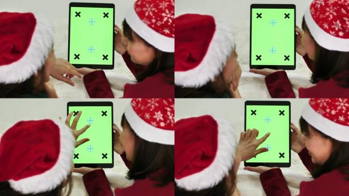 两名亚洲妇女在圣诞节使用带有绿屏的数字平板电脑