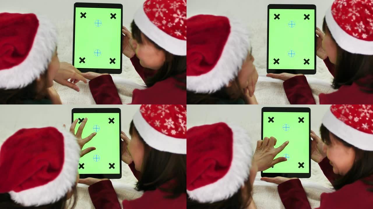 两名亚洲妇女在圣诞节使用带有绿屏的数字平板电脑