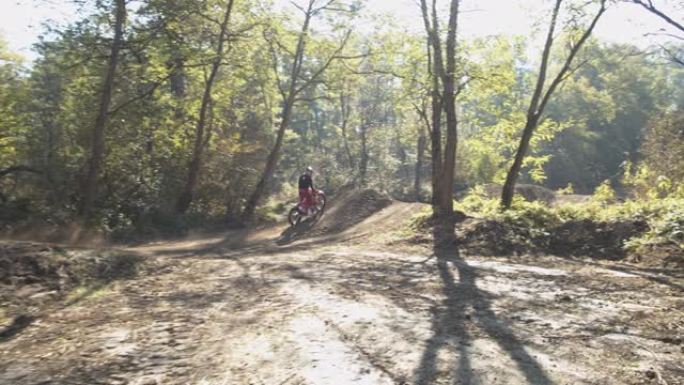 越野摩托车骑手在阳光明媚的树林中沿着泥土路线飞驰和跳跃