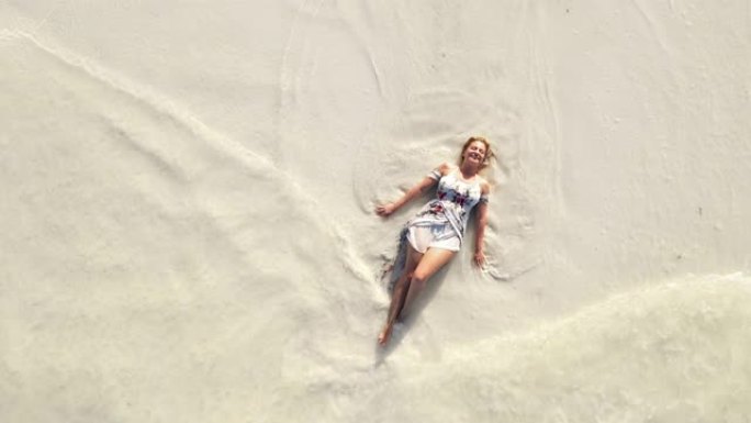 穿着太阳裙躺在沙滩上的空中快乐女人