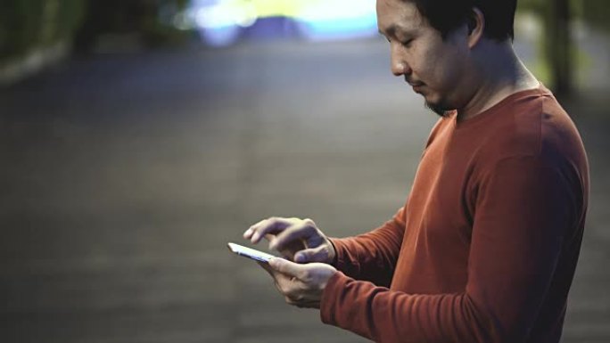 4k镜头场景亚洲男子在室外公园使用智能手机和触摸屏的特写手，带有博克照明、商业和生活方式概念