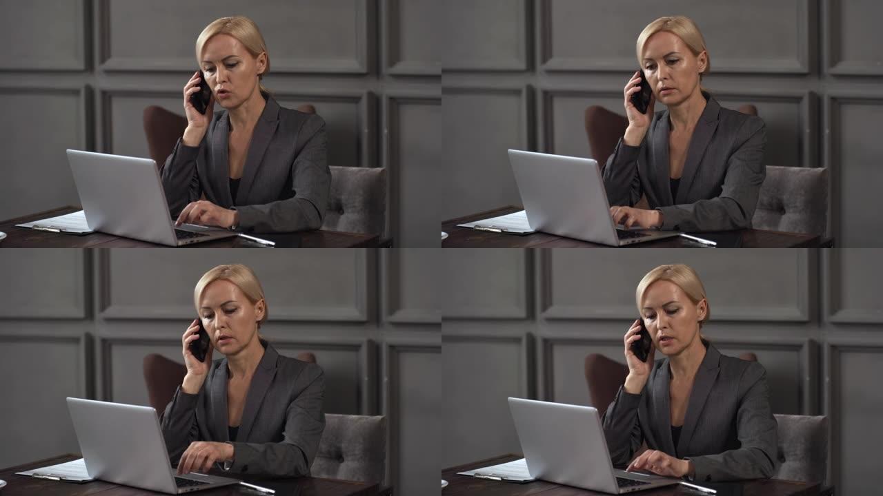 女经理在笔记本电脑上工作，并在会议期间通过电话交谈