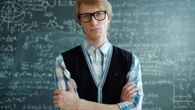 戴着眼镜的年轻人的肖像站在课堂上，严肃的脸看着相机