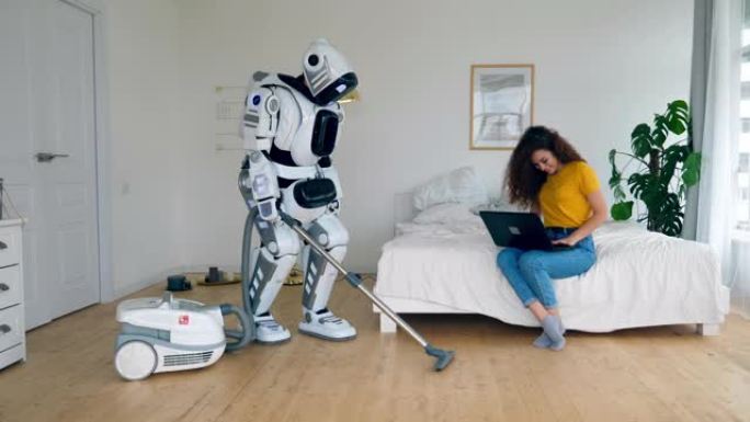 一位女士正坐在笔记本电脑上，一个机器人正在打扫卫生