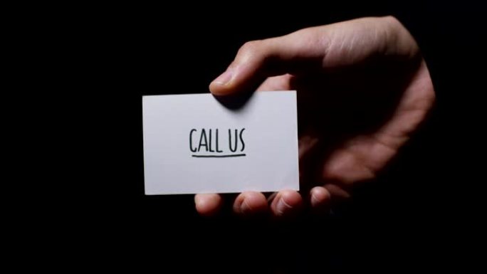 一只手显示一张卡片，上面写着: “打电话给我们”，孤立在黑色背景上。