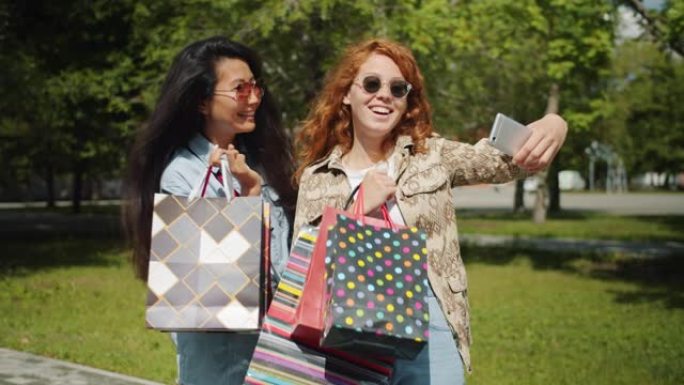 漂亮女孩在城市公园用智能手机拿着购物袋自拍