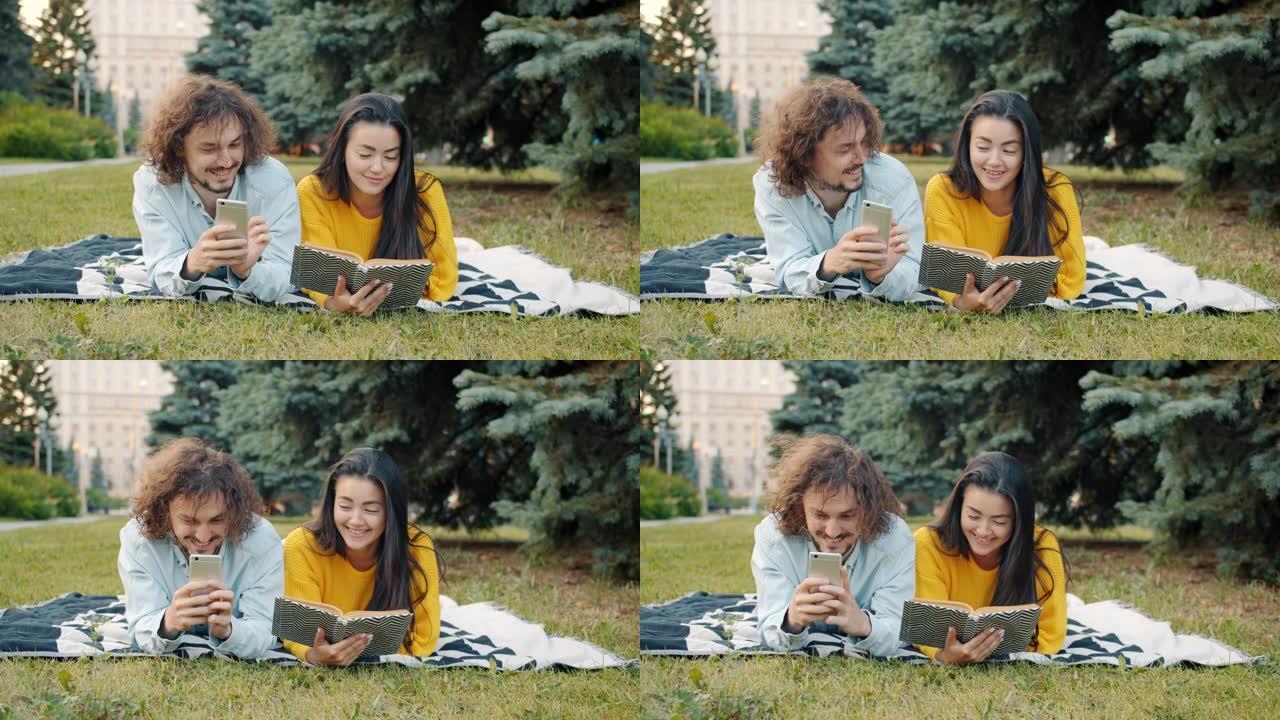 在城市公园户外放松的女孩看书时，男人使用智能手机