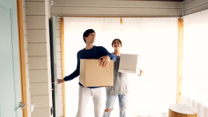 丈夫和妻子正走进新房子，并在搬迁后带来装有东西的盒子，环顾四周，微笑和亲吻。住房、青年和关系概念。