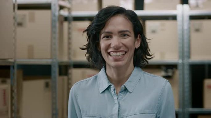 美丽的女性仓库库存经理的肖像站着，迷人地微笑着。才华横溢的职业女性与一排排装满纸箱和包裹的架子摆姿势