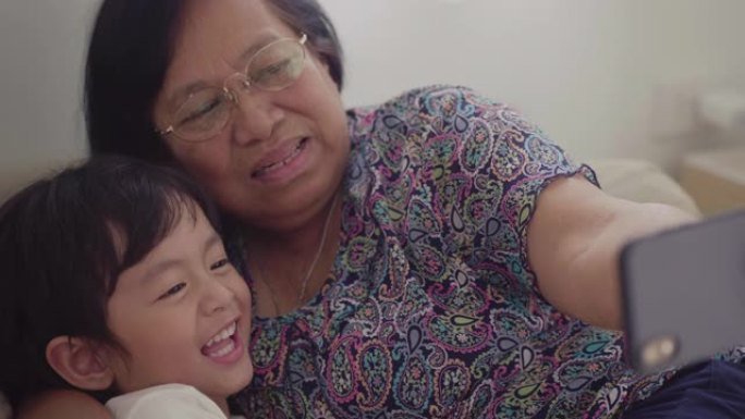 亚洲祖母和她的小男孩在家里的客厅沙发上自拍。