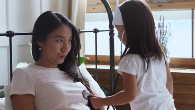 有趣的亚洲儿童女儿用听诊器扮演医生听妈妈